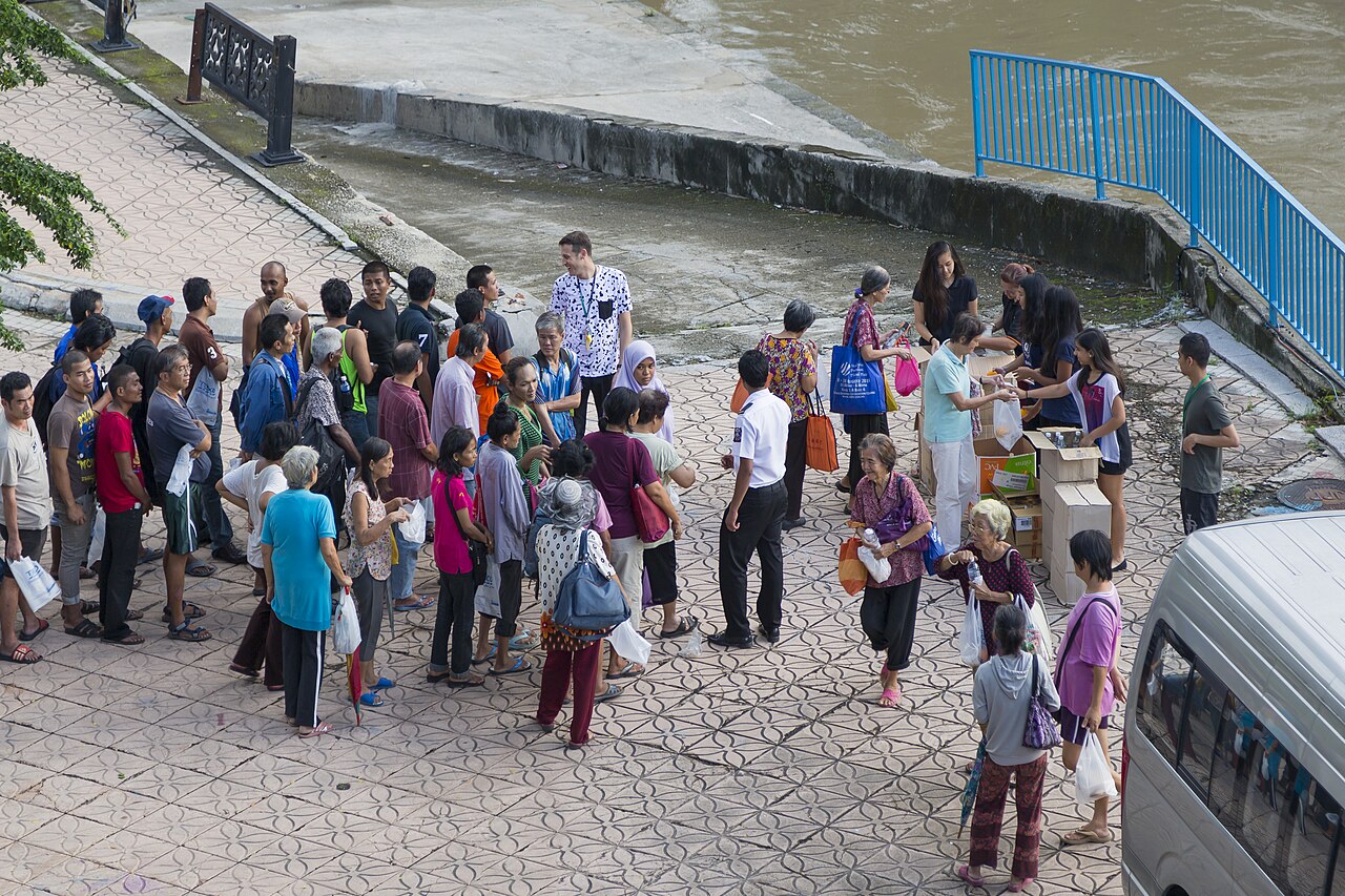 Merdeka Square at dusk with the Sultan Abdul Samad Building illuminated and Malaysian flags along the green