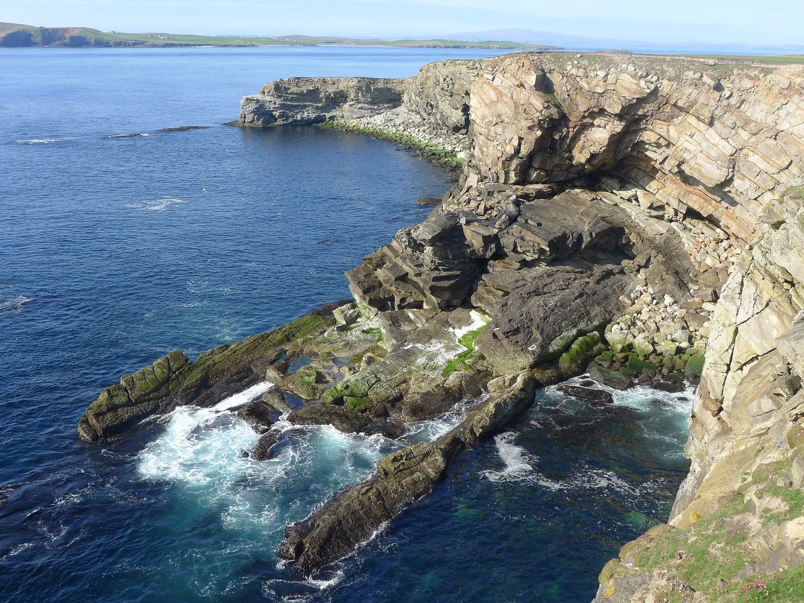 Rugged Shetland coastal cliffs with waves crashing against layered rock