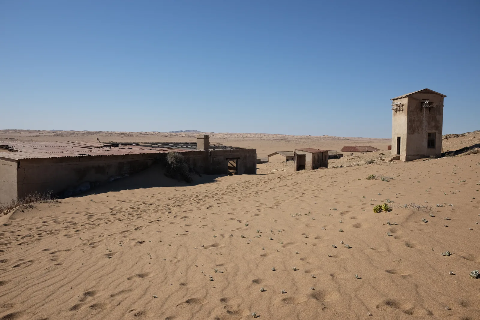 Buildings at Kolmanskop half-buried by the advancing dune field, sand drifted up to the window sills
