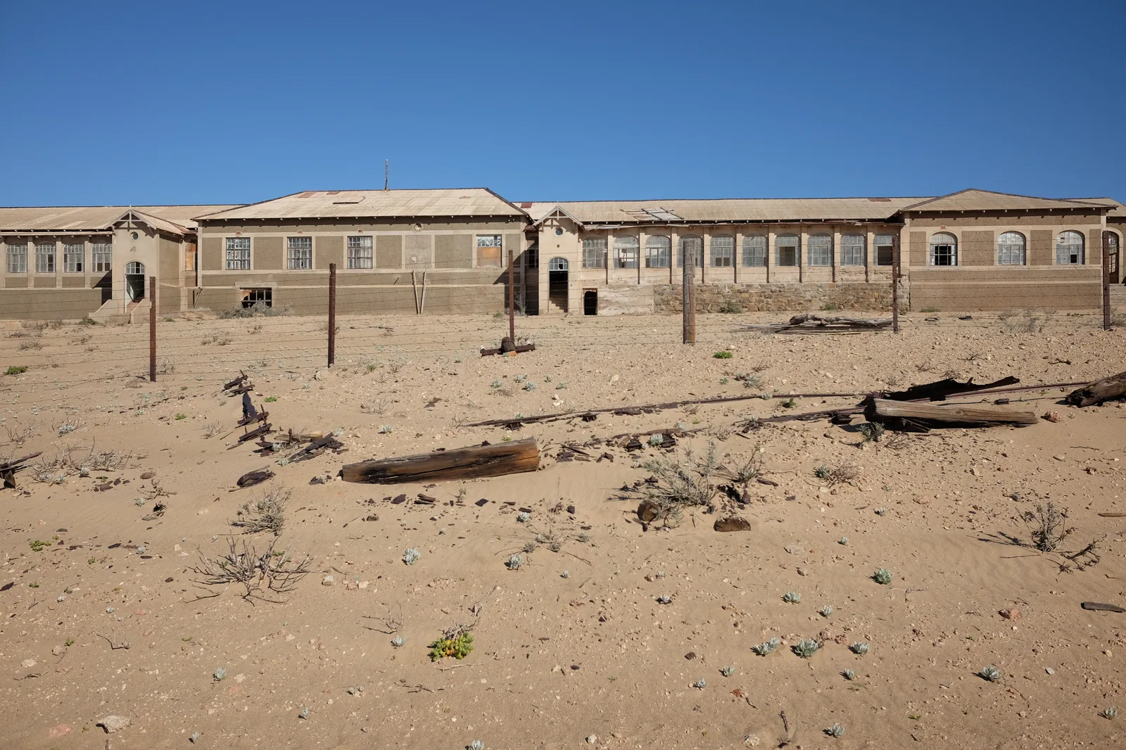 A long communal building at the abandoned mining town of Kolmanskop, its walls open and sand across the floor
