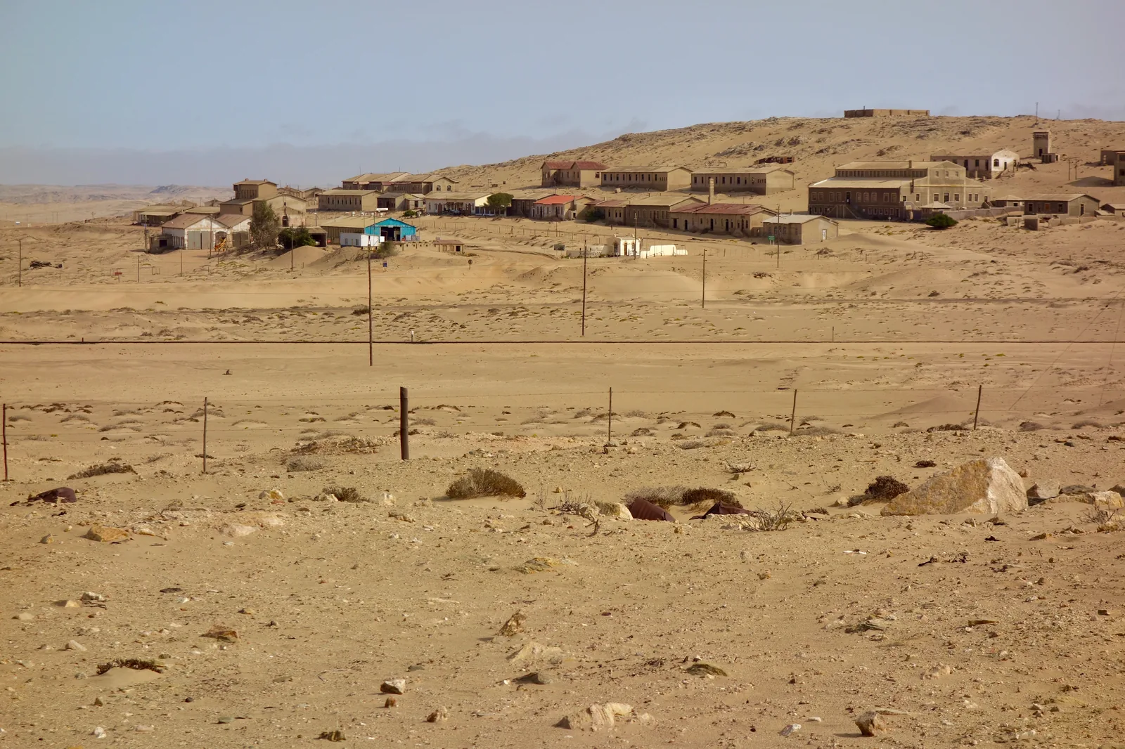 The whole ghost town of Kolmanskop strung along its dune ridge, seen from the desert plain