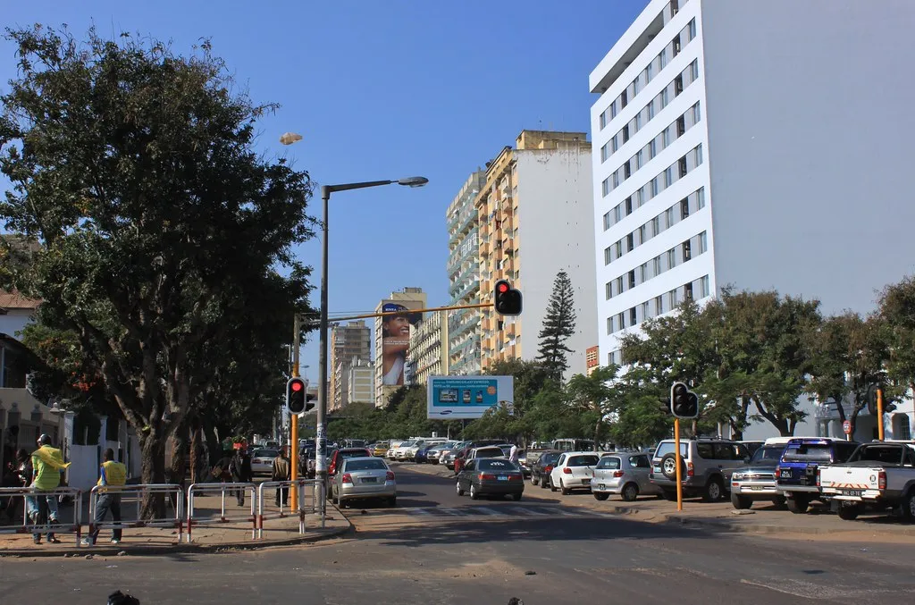 A colorful tuk-tuk three-wheeled taxi navigating a busy Maputo street with colonial buildings in background