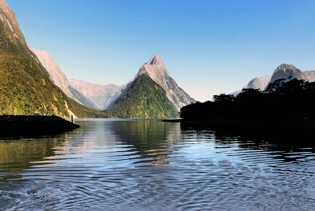 Mitre Peak rising sharply from the calm waters of Milford Sound with mountains reflected in the fiord