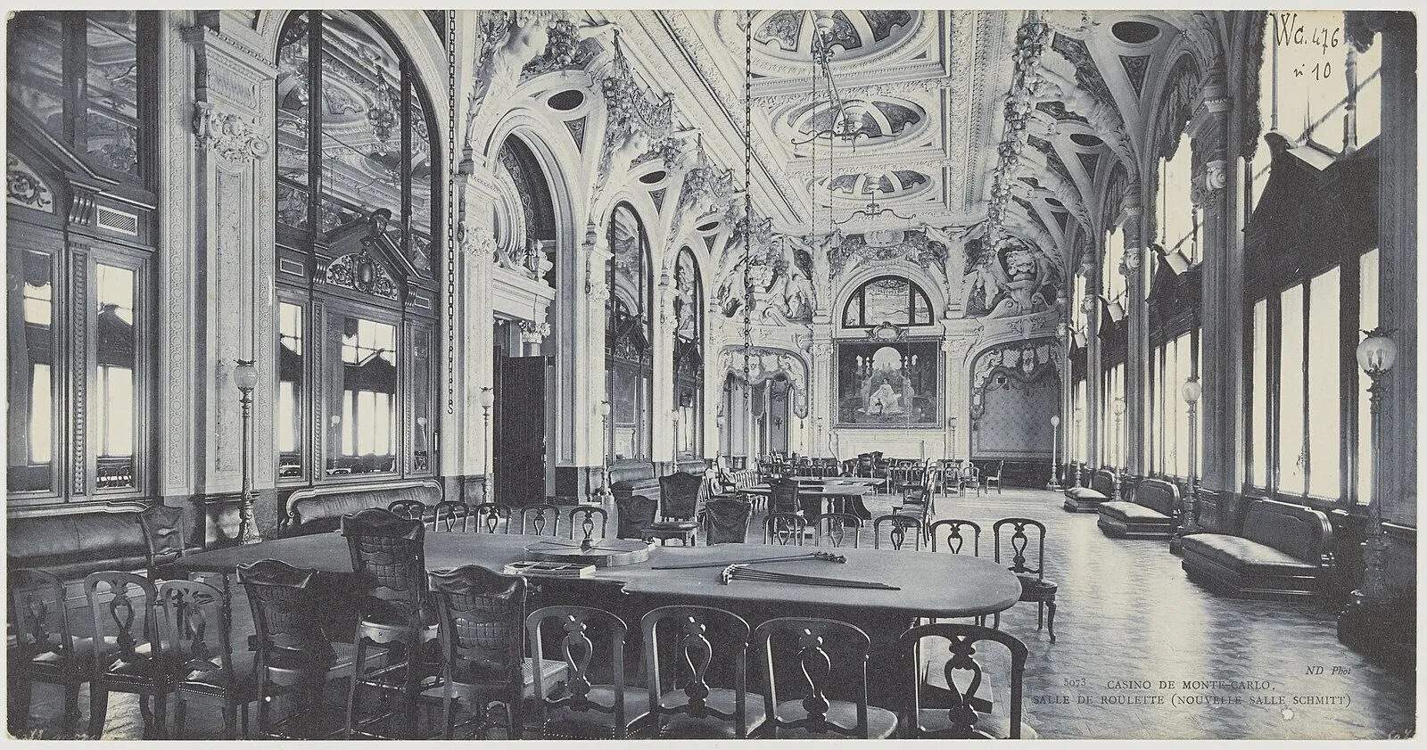 Historical black and white interior of Casino de Monte-Carlo gaming room with ornate ceiling and roulette tables