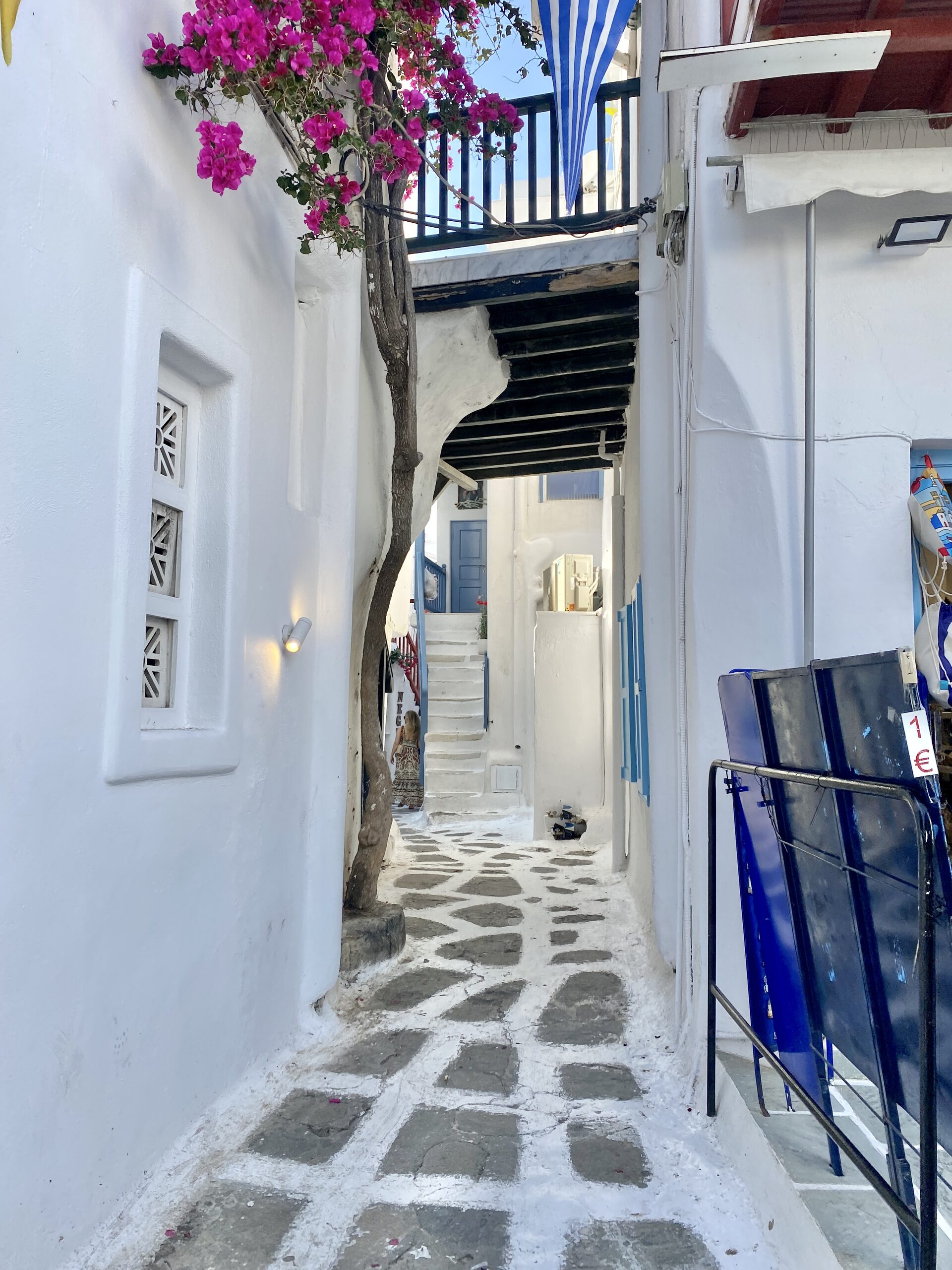 Narrow whitewashed alley in Mykonos with purple bougainvillea and cobblestone path