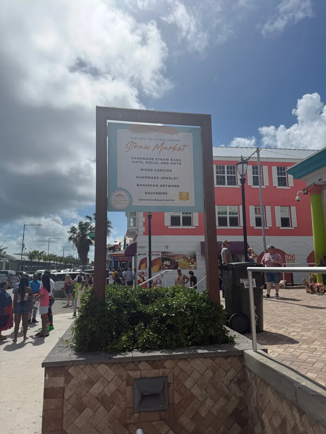 Straw Market entrance sign at Prince George Wharf — sponsored by Nassau Cruise Port, listing handmade straw bags, hats, dolls, wood carving, handmade jewelry, Bahamian artwork, and souvenirs under the Made in the Bahamas stamp