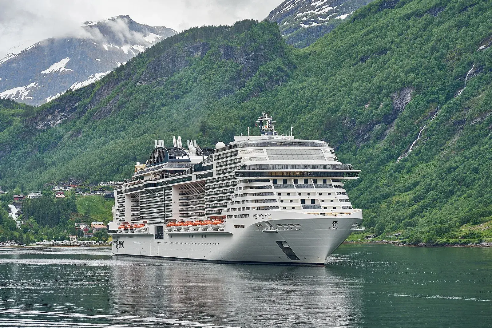 Panoramic view from Flydalsjuvet viewpoint showing a cruise ship far below in the deep blue fjord waters