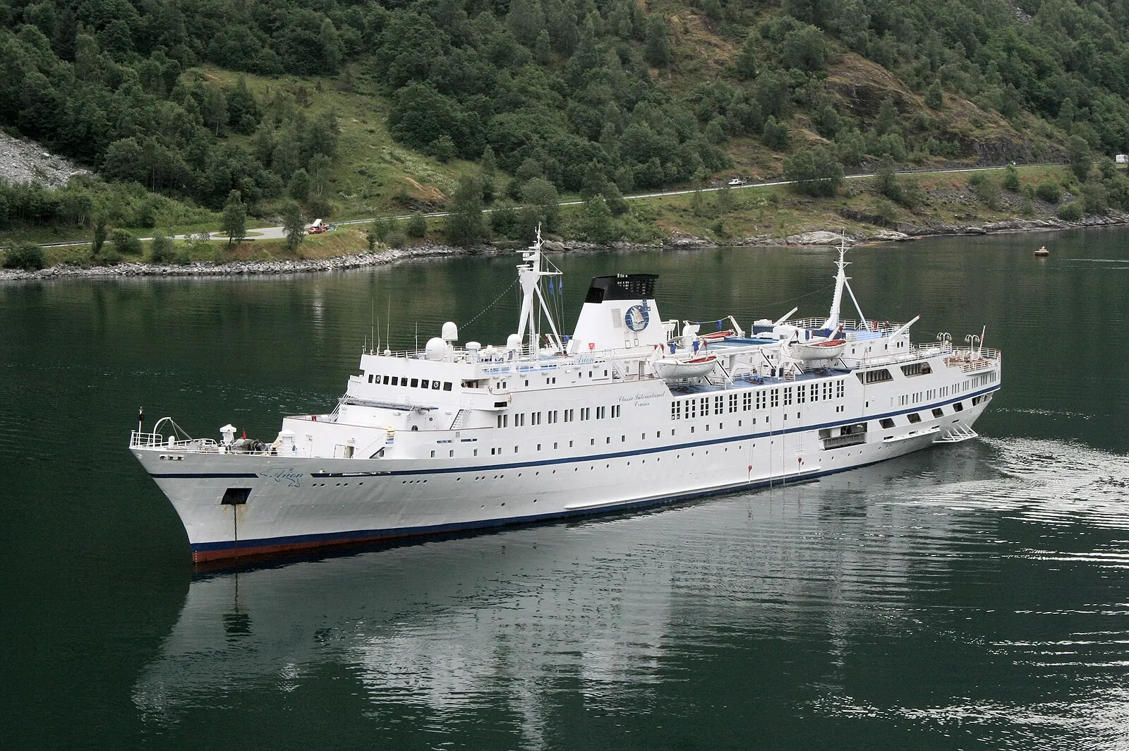 A historic wooden stave church surrounded by green hillsides and mountains in the Norwegian countryside