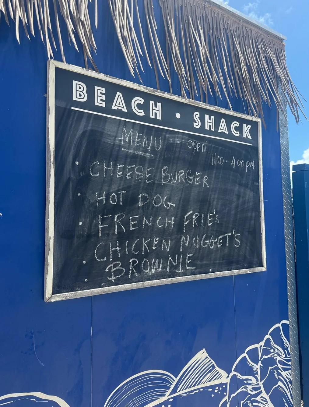 Hand-chalked menu board at the Ocean Cay Beach Shack: cheeseburger, hot dog, French fries, chicken nuggets, brownie, open 11 to 4