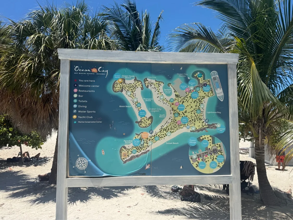 Wide framed view of the Ocean Cay island-map signboard at the beach edge, palm trees flanking it