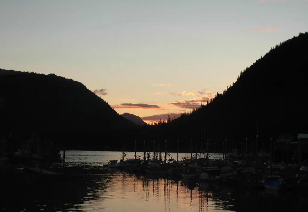 Sunset over Petersburg harbor with silhouetted mountains and fishing boats reflected in calm water