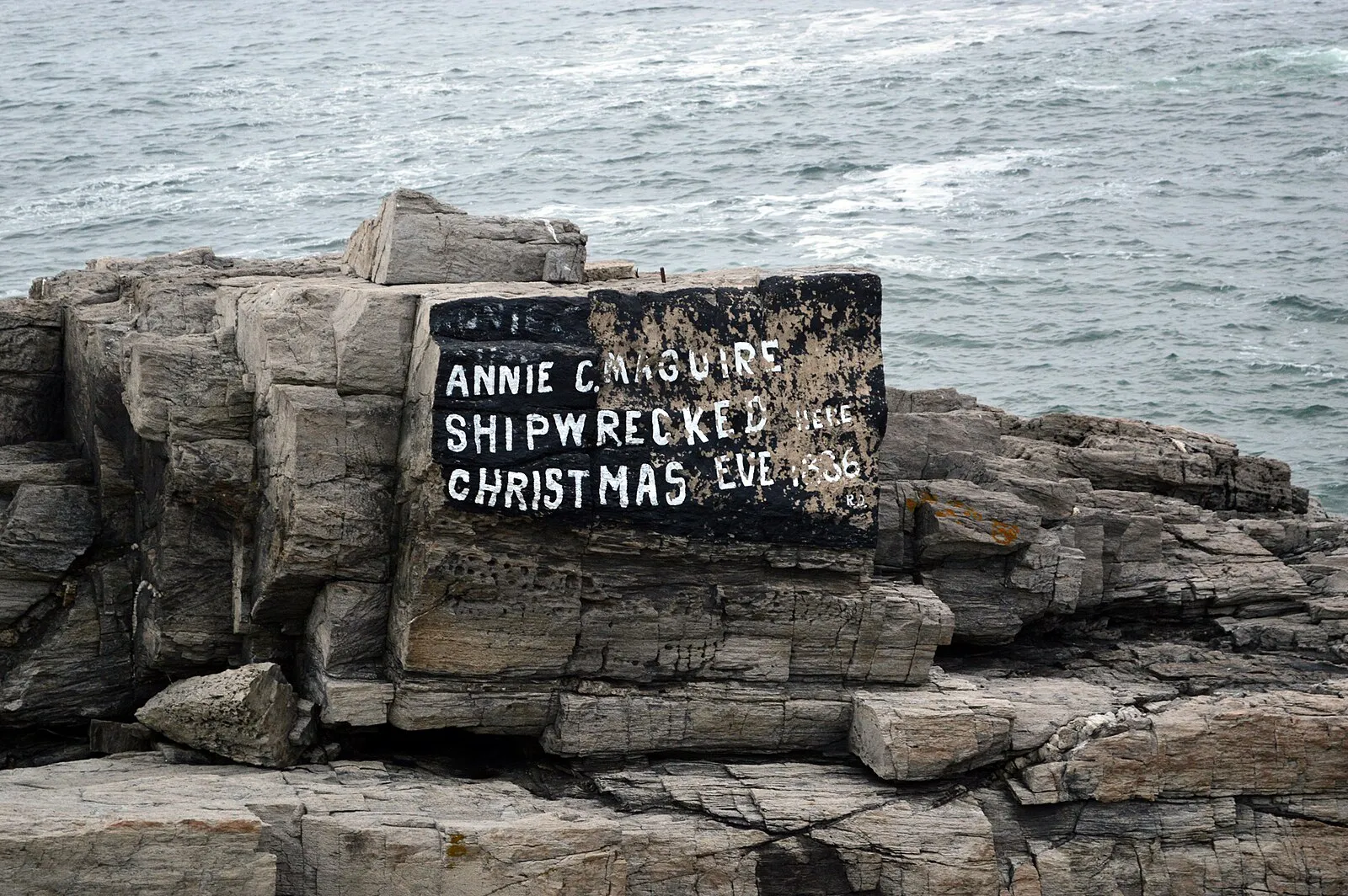 Portland Head Light lighthouse at golden hour with dramatic waves crashing on granite rocks below the white tower