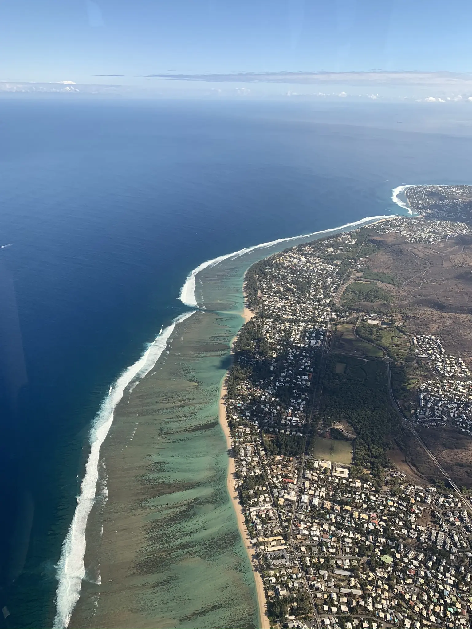The turquoise lagoon at L'Hermitage seen from a helicopter, held inside a pale fringing coral reef with dark ocean beyond