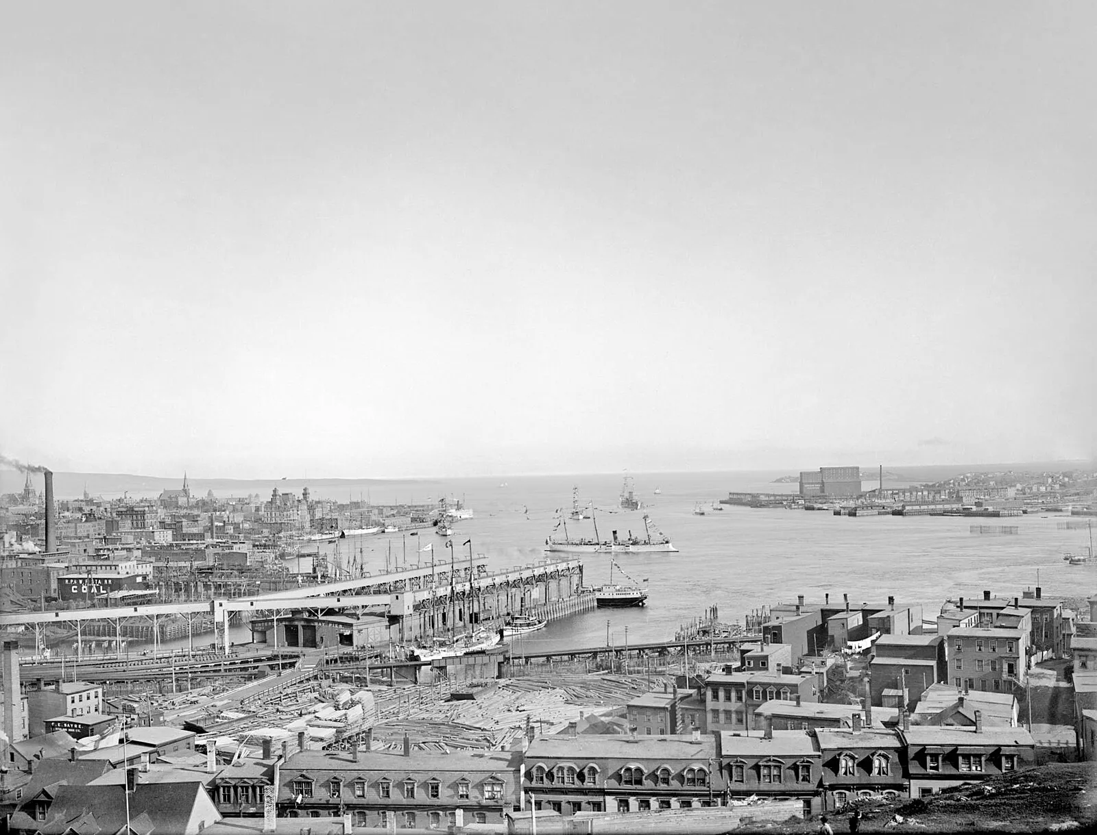 Historical black and white panoramic view of Saint John harbour with wharves and ships