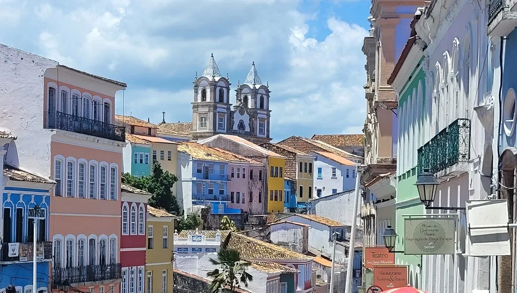 A Baiana woman in traditional white lace dress and headwrap frying acaraje black-eyed pea fritters in a large pan of palm oil at a street stall