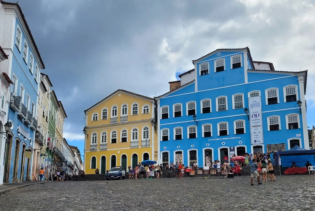 White facade of the Igreja do Nosso Senhor do Bonfim with colorful ribbon wish bracelets tied to the iron fence in the foreground