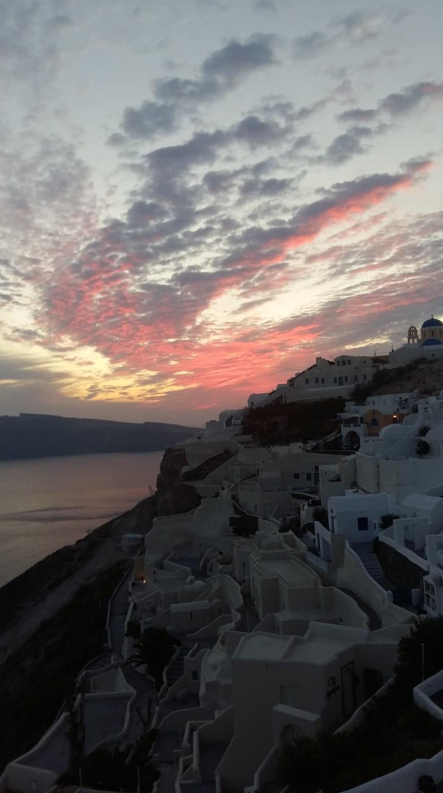 Sunset over Oia village with whitewashed buildings and blue-domed church on the caldera rim
