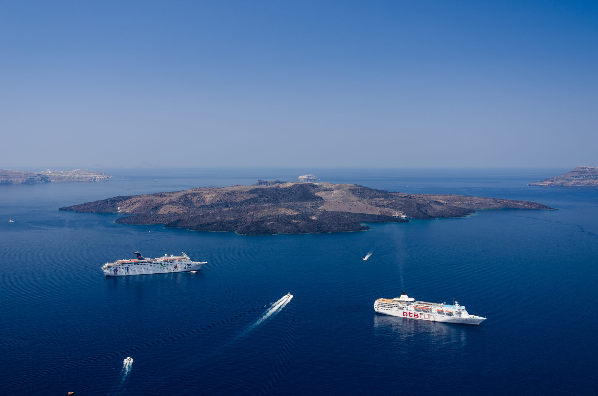 Panoramic view of cruise ships anchored in Santorini caldera with Nea Kameni volcanic island in center
