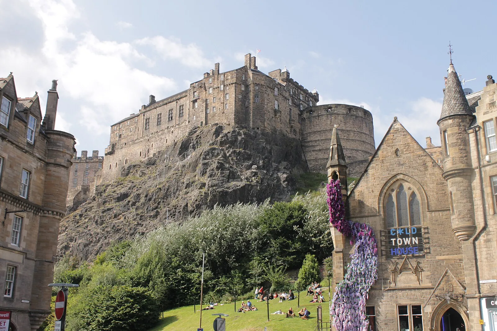 Edinburgh Castle from the Grassmarket park area with people relaxing on the grass below the castle rock