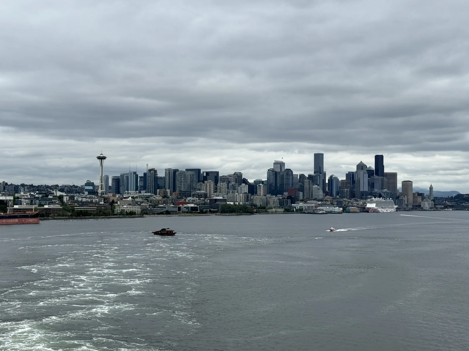 The Seattle skyline from Elliott Bay — Space Needle at left, downtown towers at centre, a cruise ship at the downtown waterfront and the Seattle Great Wheel at right