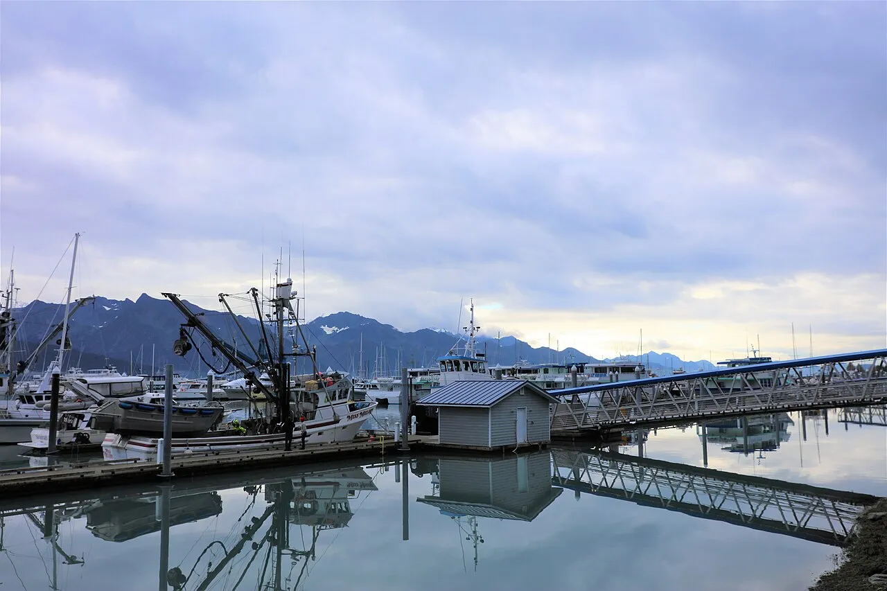 Seward Small Boat Harbor at dusk with fishing vessels, docks, and Kenai Mountains reflected in calm water