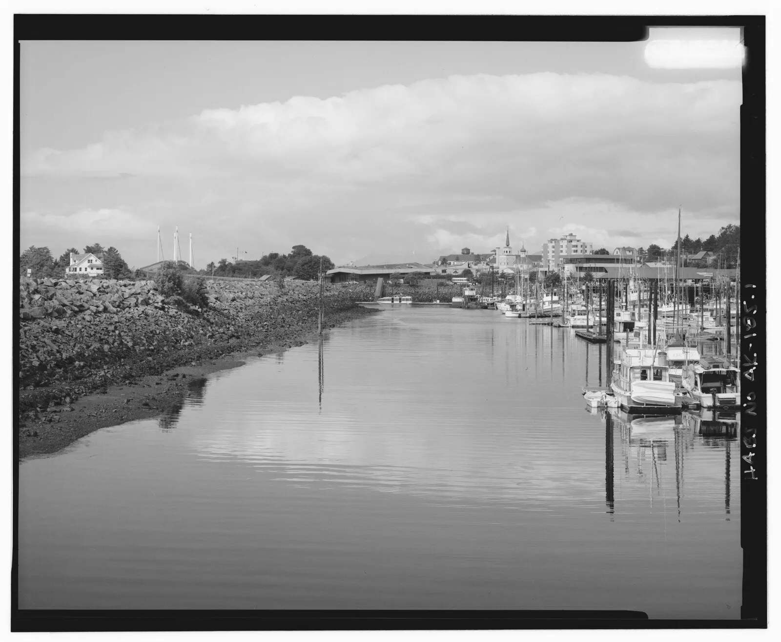 Historical HAER black and white photo of Sitka harbor with boats, rocky shores, church steeple, and town