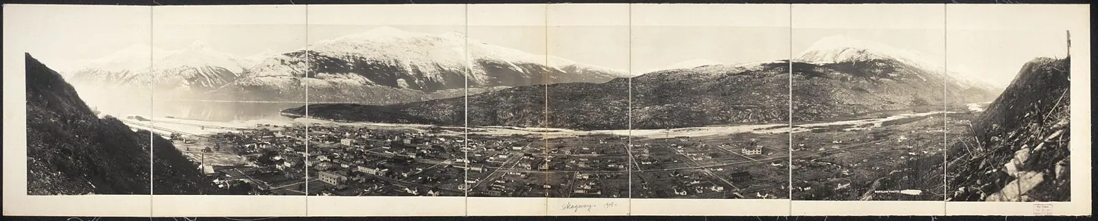 Historic multi-panel panoramic photograph of entire Skagway town with mountains, Lynn Canal, and snow-capped peaks