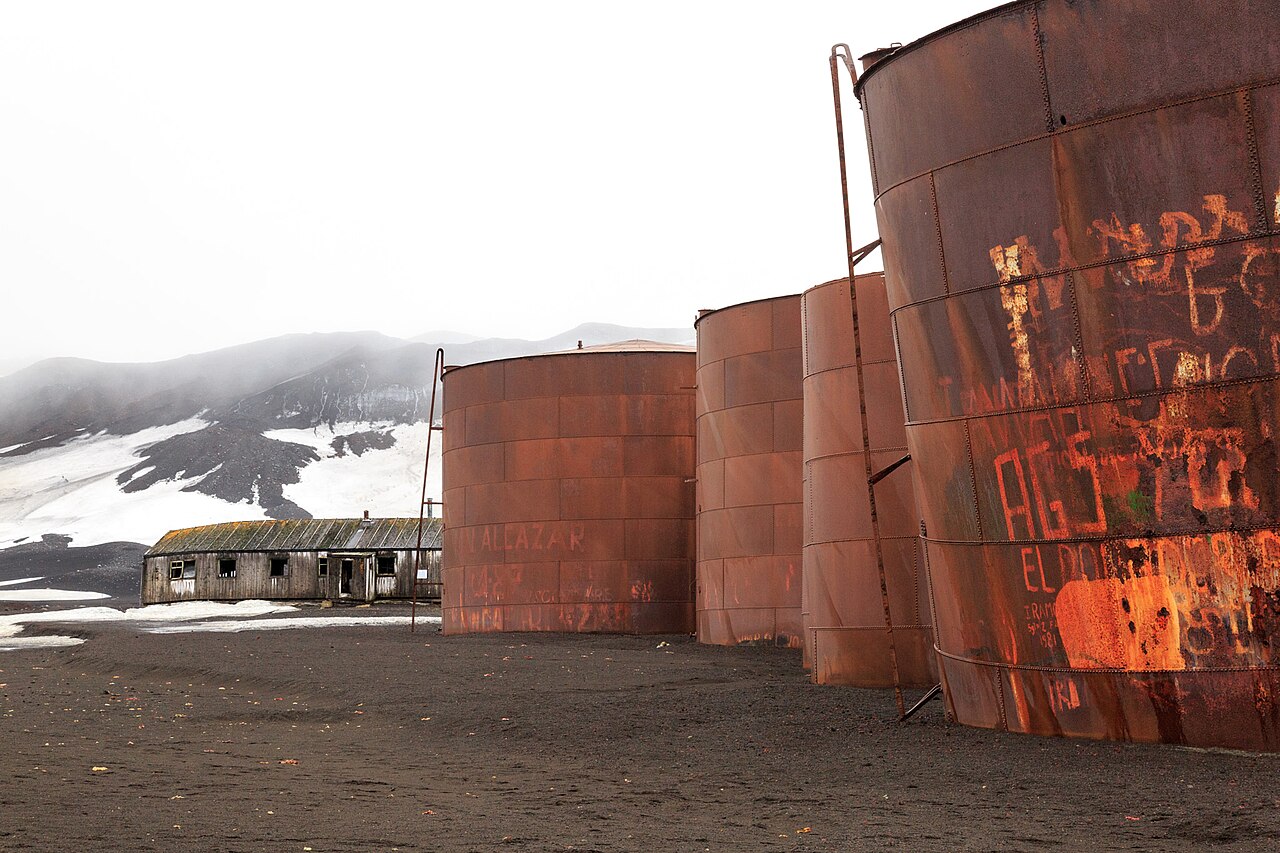 Rusting whale oil storage tanks at abandoned Whalers Bay whaling station, Deception Island, with volcanic ash slopes