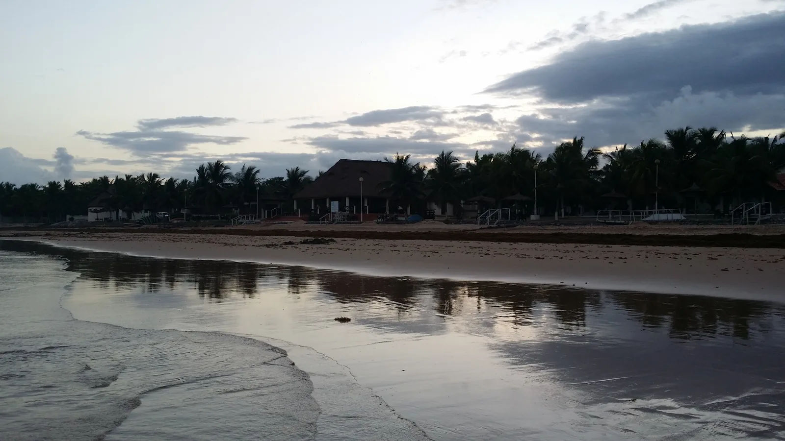Busua Beach in Ghana's Western Region on an overcast day, surf running up a wide sand beach