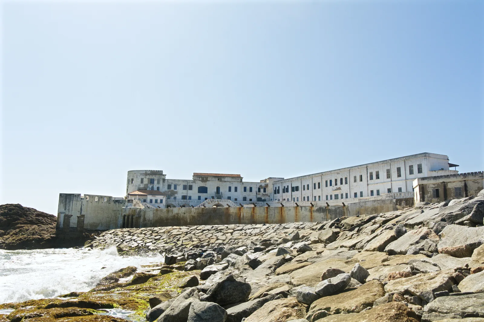 Cape Coast Castle, the whitewashed fortress on Ghana's southern coast, seen from the shore in daylight