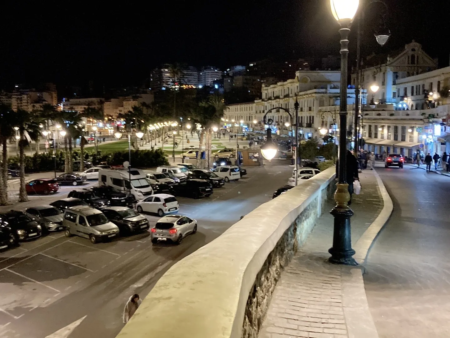 Tangier waterfront at night with colonial buildings, palm trees, and hillside city lights