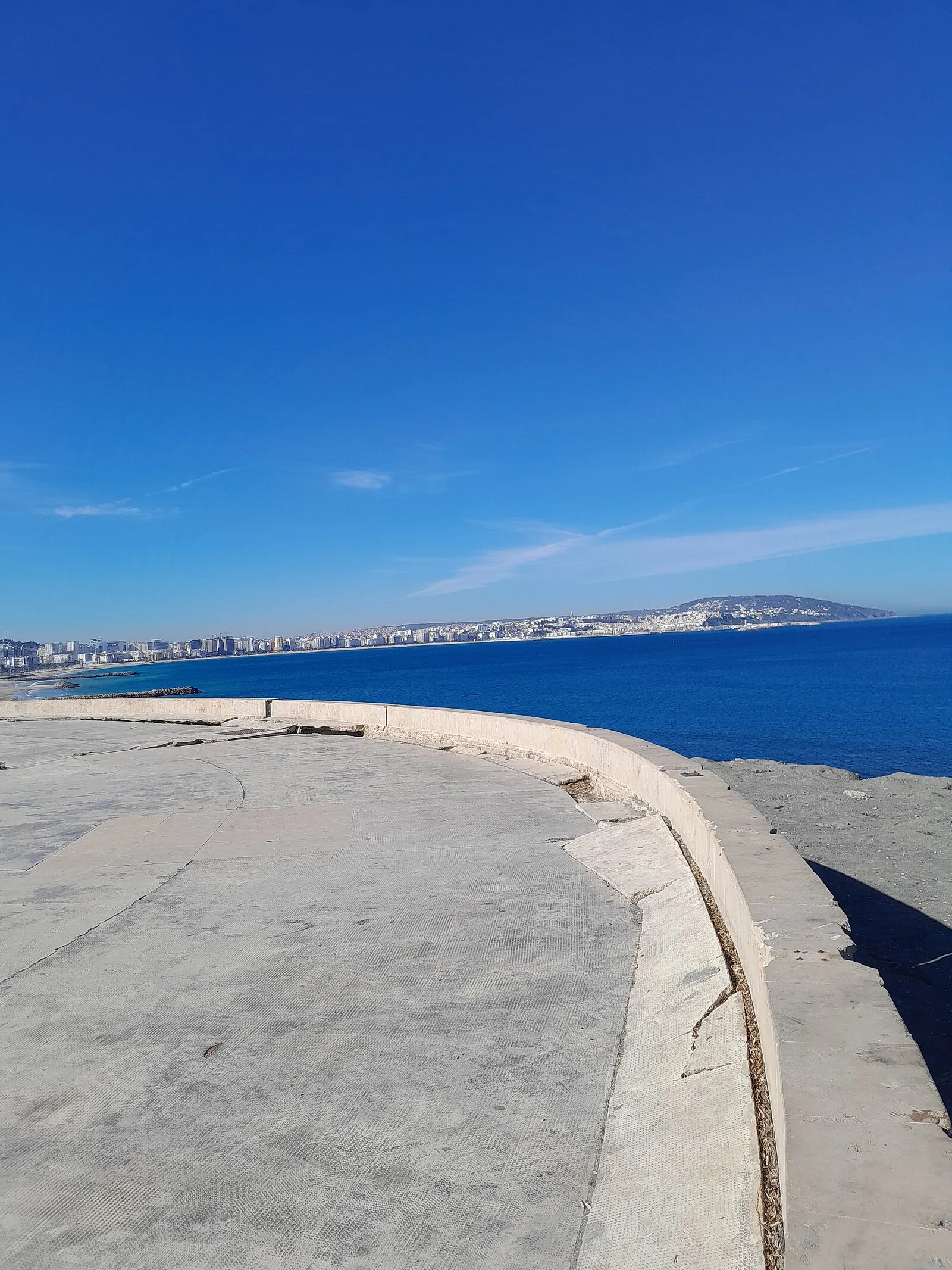 Tangier coastline from concrete breakwater with deep blue Mediterranean Sea and city skyline
