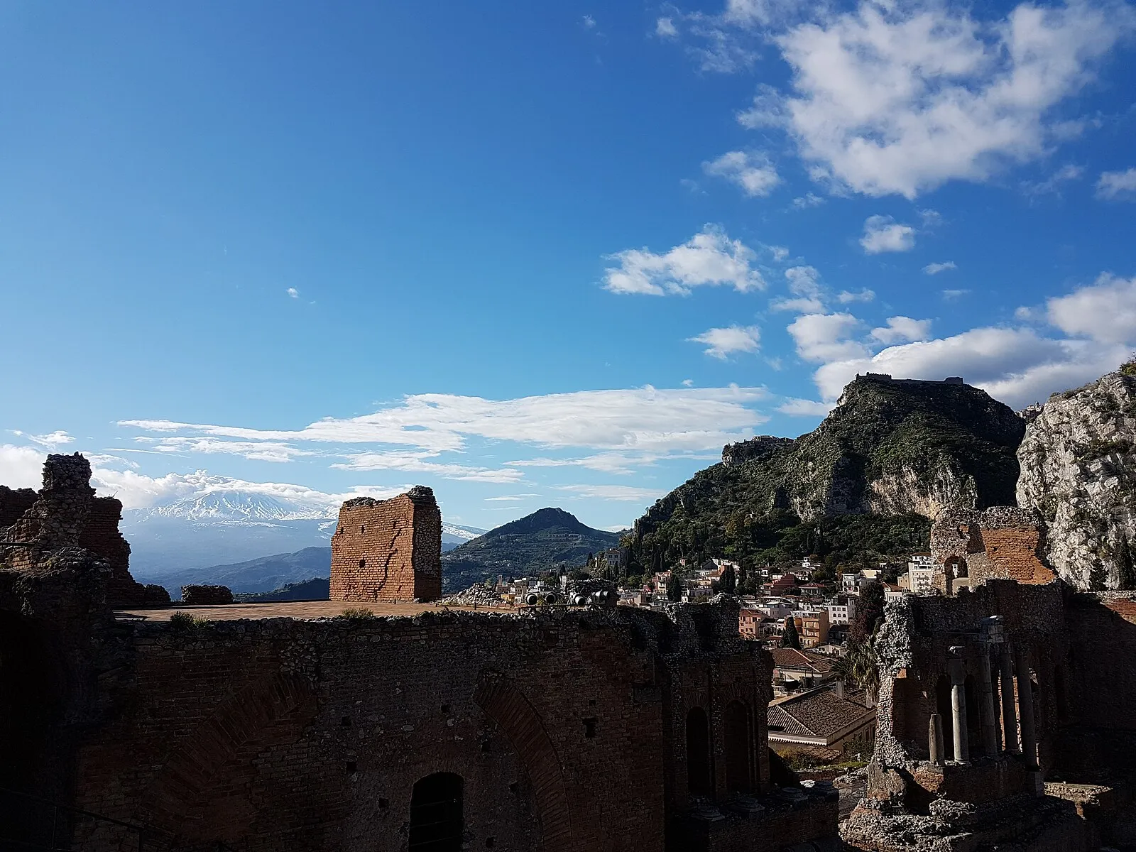 Teatro Greco di Taormina ruins with snow-capped Mount Etna and hilltop town