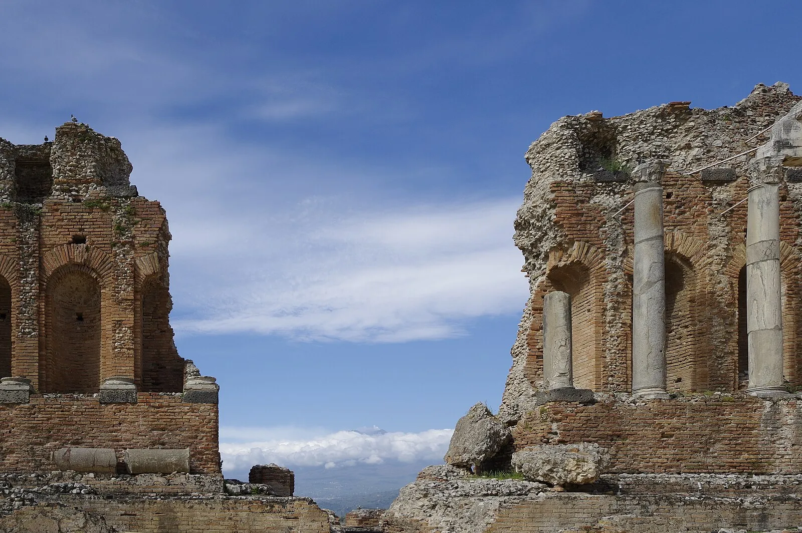 Teatro Greco di Taormina stage wall ruins with gap showing clouds and mountainous backdrop