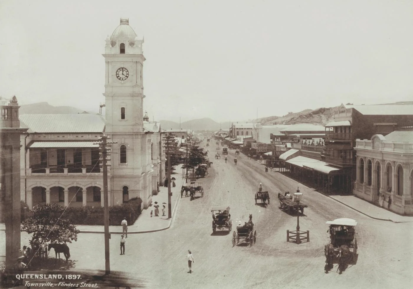 Sepia photograph from 1897 looking down Flinders Street, Townsville, past the post office clock tower with horse cabs and verandahed shopfronts