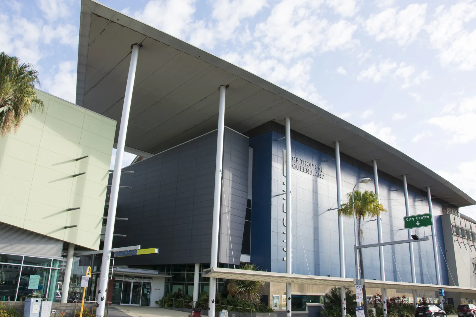 The Queensland Museum Tropics building on Flinders Street, Townsville, its grey and blue facade seen from below with the name on the wall