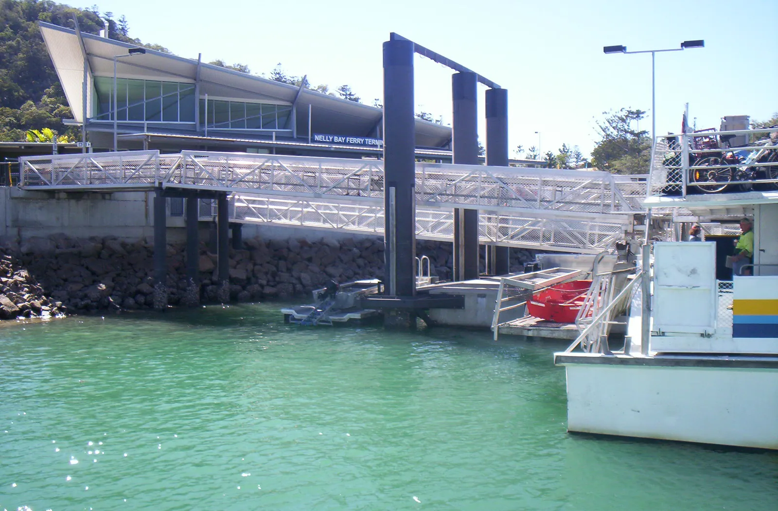 Nelly Bay Ferry Terminal on Magnetic Island with an aluminium gangway and the white bow of a berthed ferry over green water