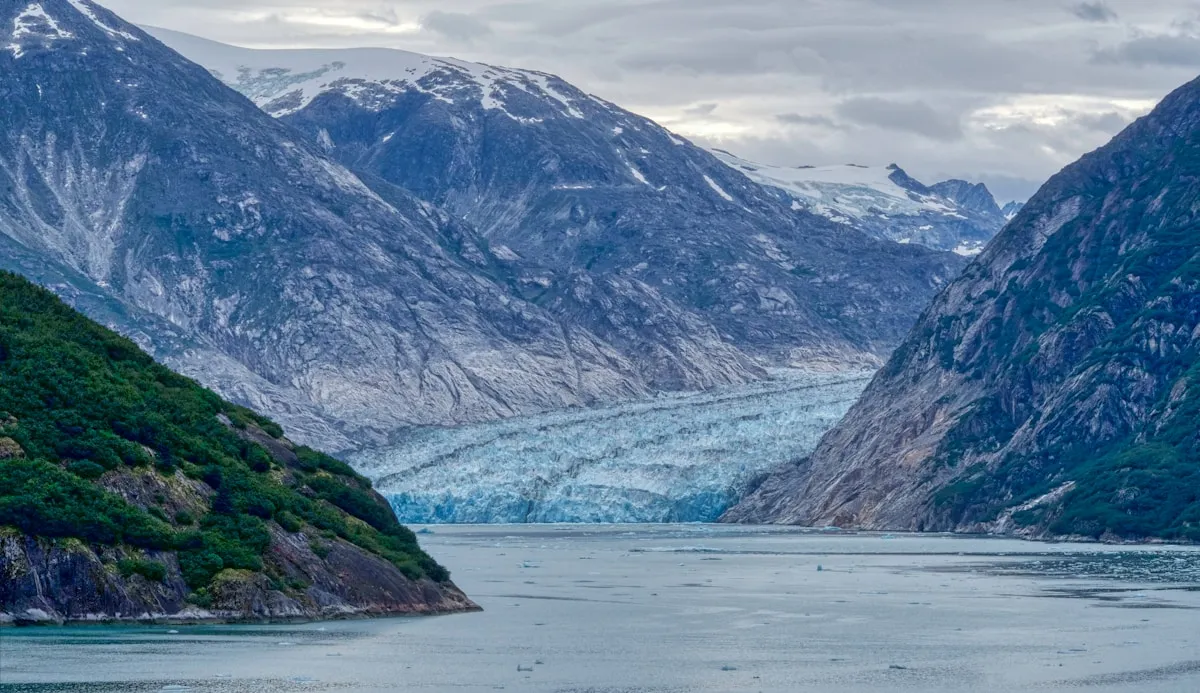 Tracy Arm Fjord approach with the blue face of Sawyer Glacier visible between steep mountain walls, floating ice on the water surface