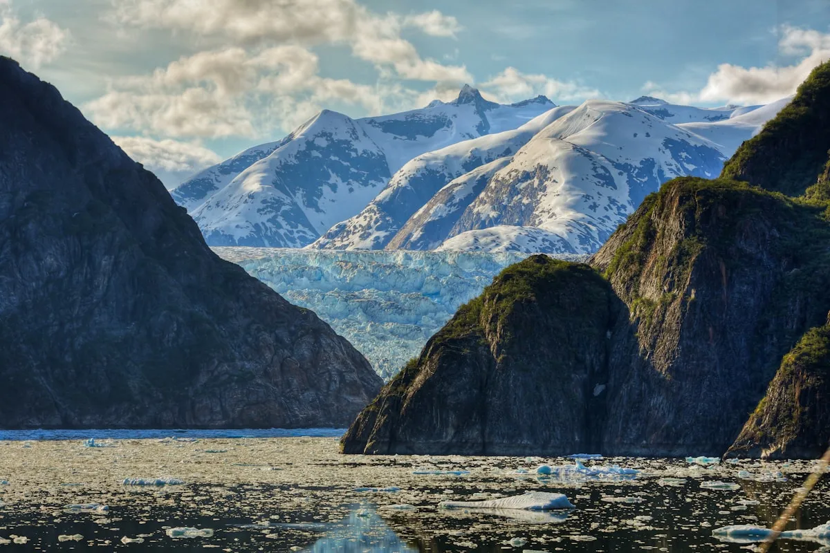 Tracy Arm Fjord with Sawyer Glacier visible through steep granite walls, ice chunks floating in turquoise water, snow-capped peaks above