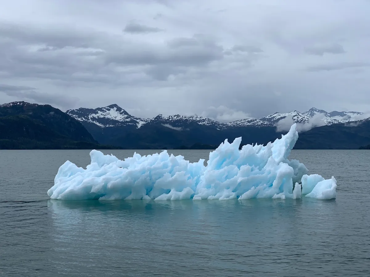 Blue iceberg from the Columbia Glacier floating in Prince William Sound with snow-capped Chugach Mountains in the background