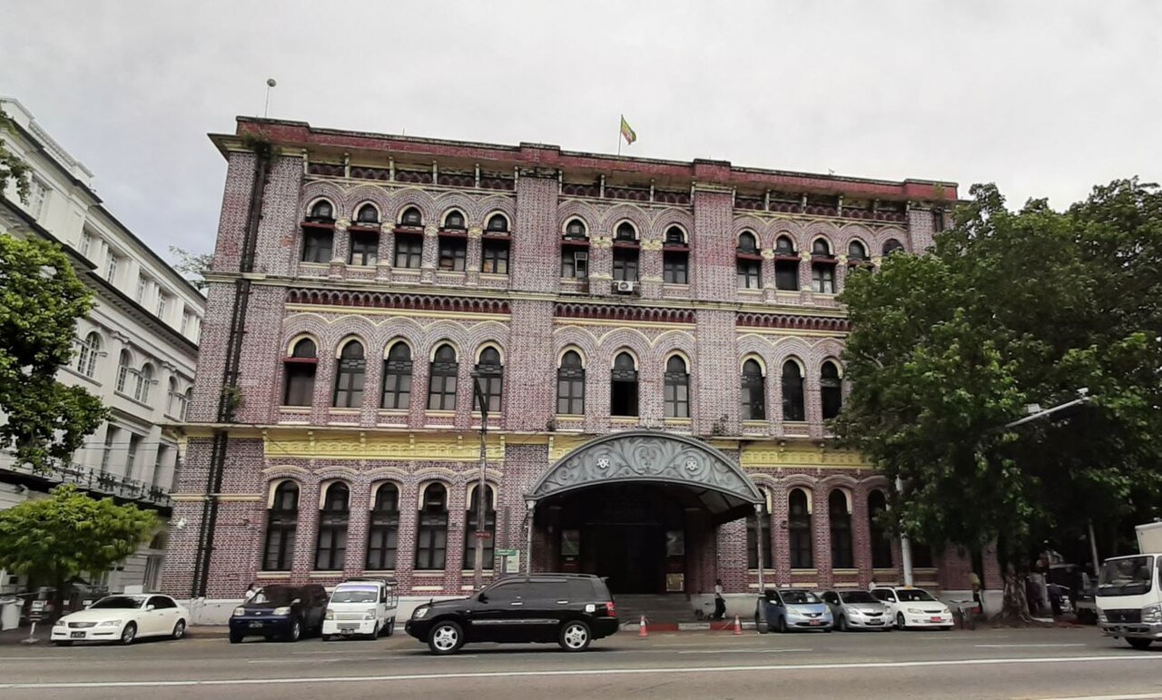 The golden spire of Shwedagon Pagoda gleaming at sunset with devotees walking the marble platform below