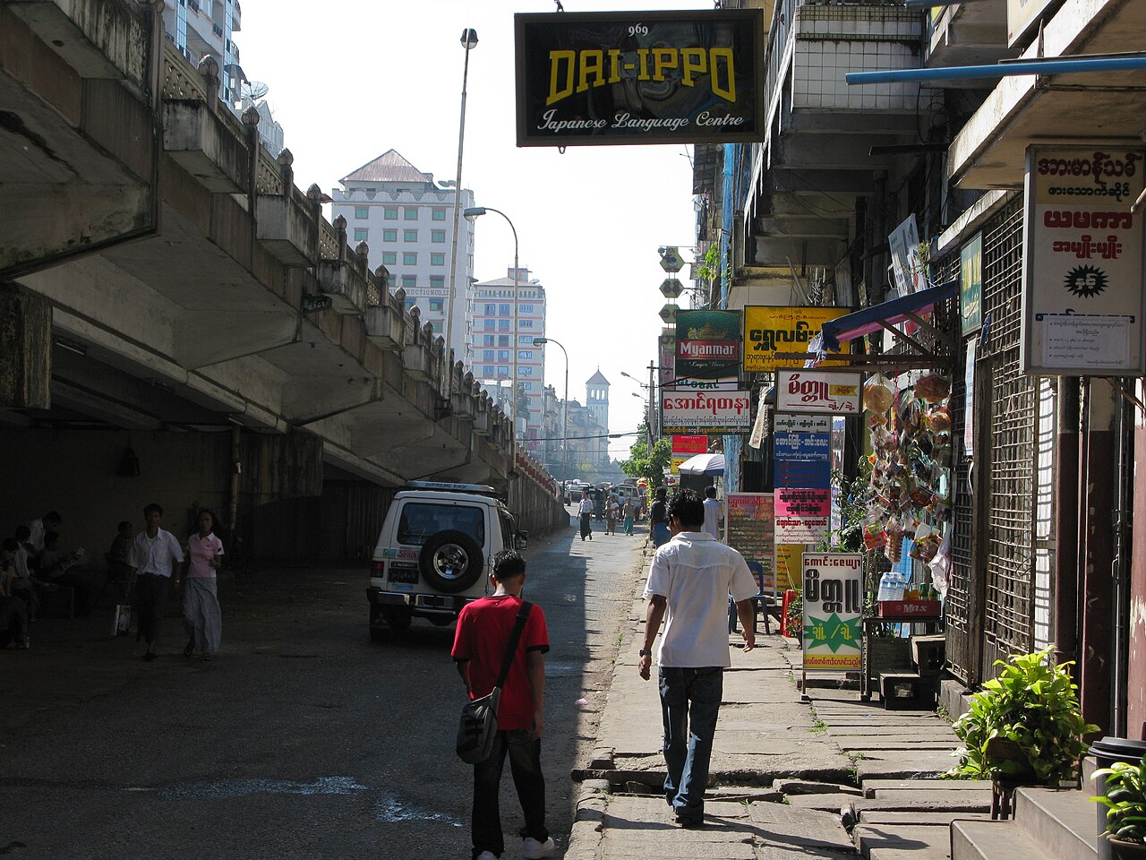 Busy street scene in downtown Yangon with colonial buildings, pedestrians, and traditional market stalls