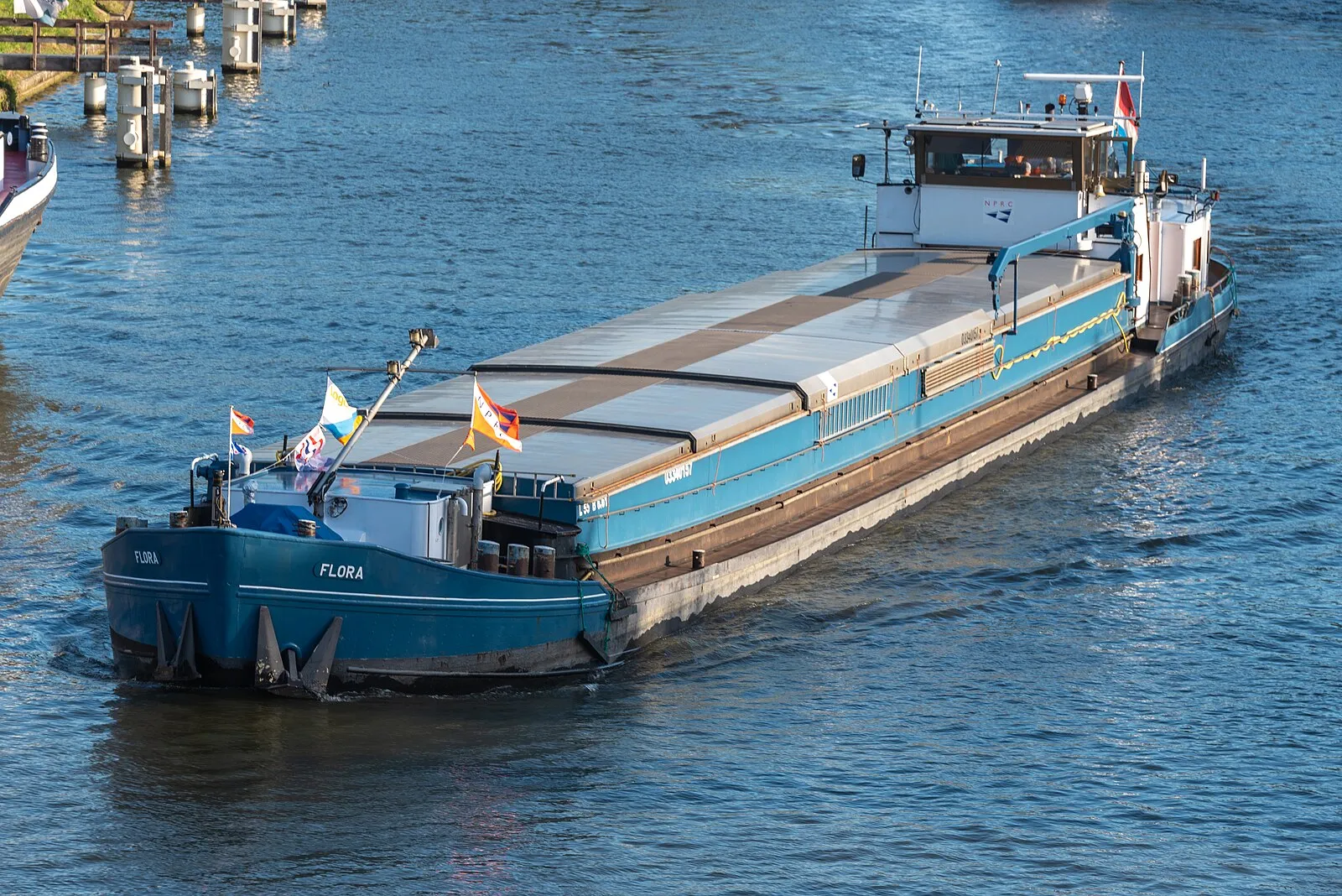 Blue cargo barge Flora navigating a Belgian canal near Bruges