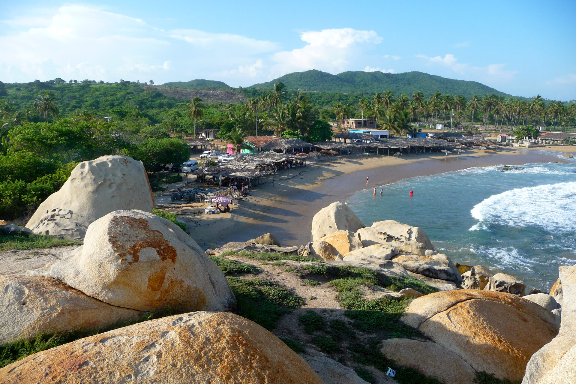 Curved golden sand of Playa La Ropa beach in Zihuatanejo with palm trees, fishing boats, and green hillsides embracing the sheltered bay